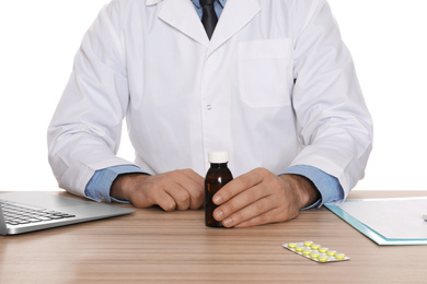 Professional pharmacist with syrup and laptop at table against white background, closeup