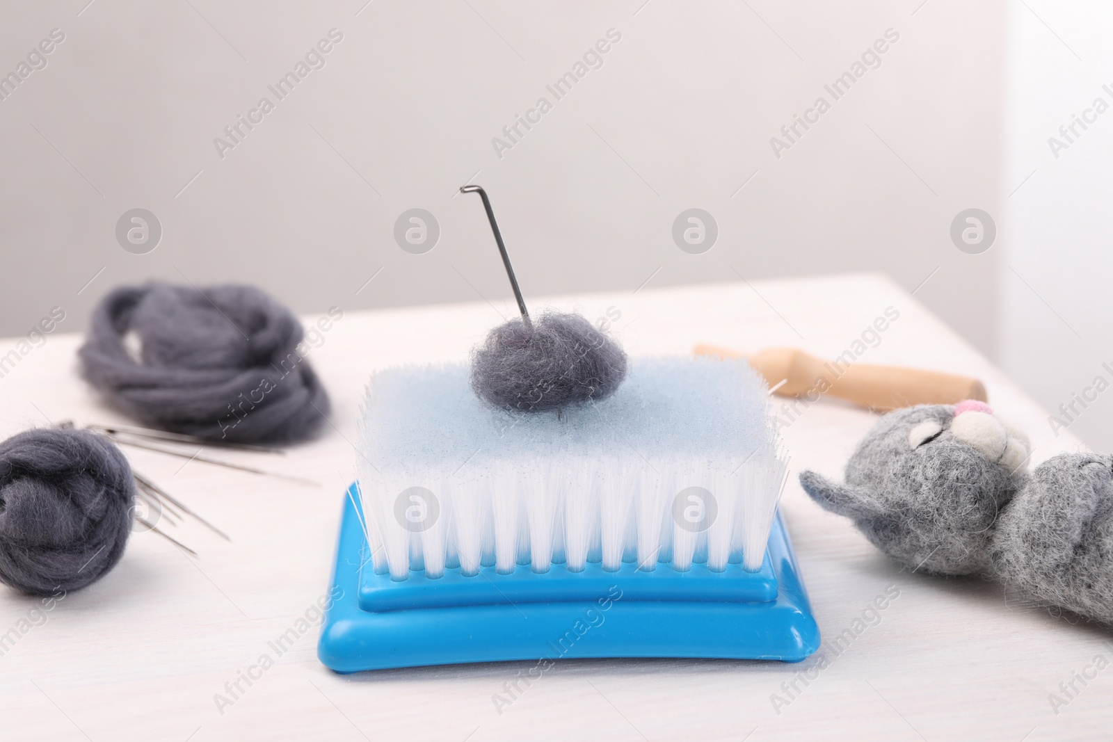 Photo of Felting tools, wool and toy cat on light wooden table, closeup