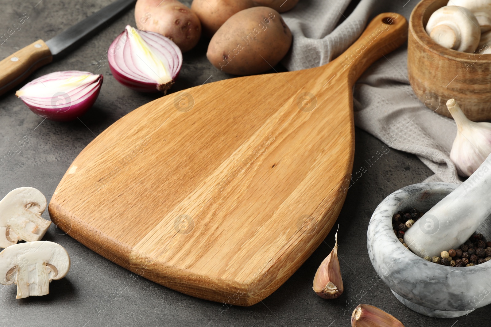 Photo of Wooden cutting board and products on dark textured table, closeup