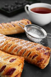 Photo of Fresh tasty puff pastry with sugar powder served on grey table, closeup