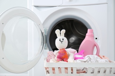 Photo of Bottle of detergent, toy and children's clothes in basket near washing machine