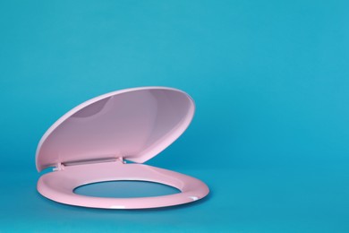 Photo of New pink plastic toilet seat on light blue background, space for text
