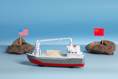 Photo of Toy cargo vessel, stones with American and Chinese flags on color background. Export concept