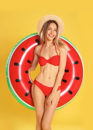 Beautiful young woman in stylish bikini with watermelon inflatable ring on yellow background