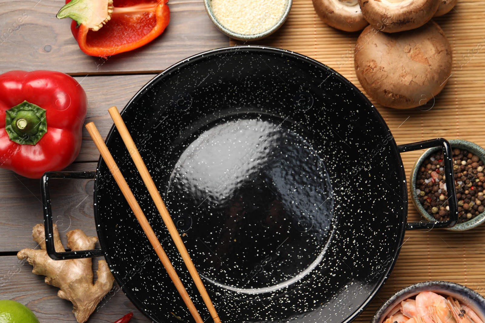 Photo of Black wok, chopsticks and products on color wooden table, flat lay