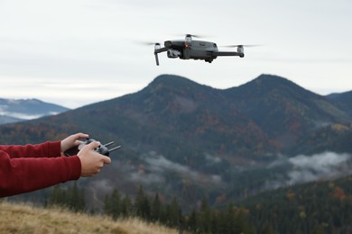Photo of Man operating modern drone with remote control in mountains, closeup. Space for text