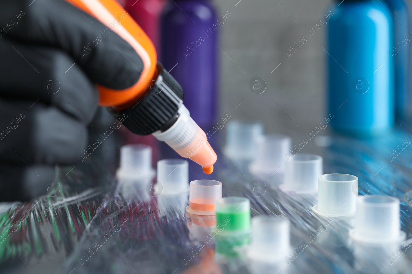 Photo of Tattoo artist dripping orange tattoo ink into cap on table, closeup