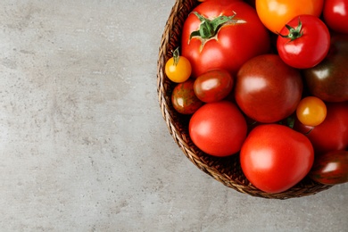 Fresh ripe tomatoes in wicker bowl on grey table, top view. Space for text