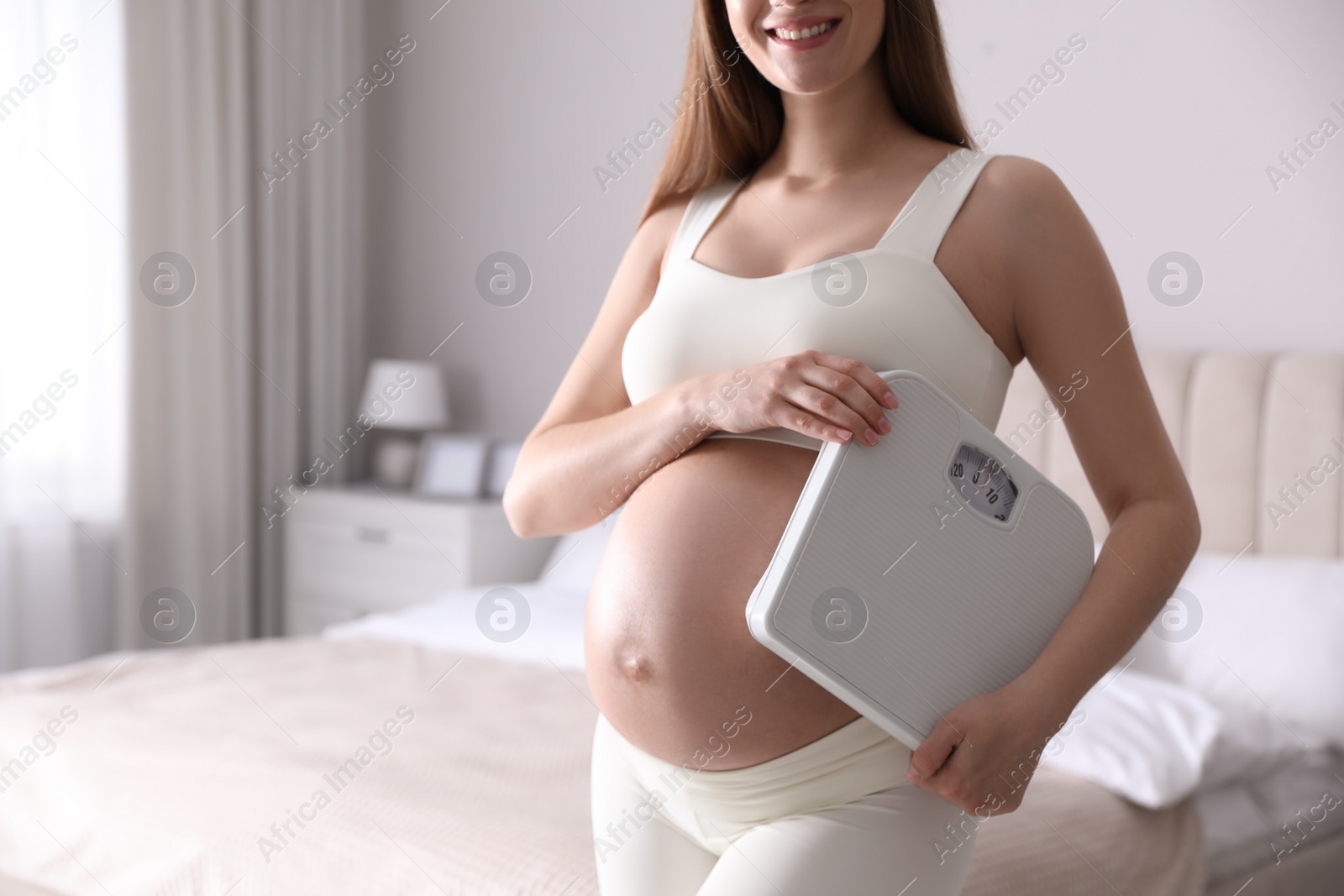 Photo of Young pregnant woman with scales in bedroom, closeup