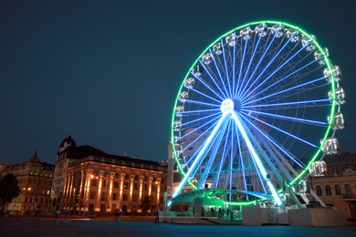 Photo of Big Ferris wheel on city street at night, low angle view. Space for text