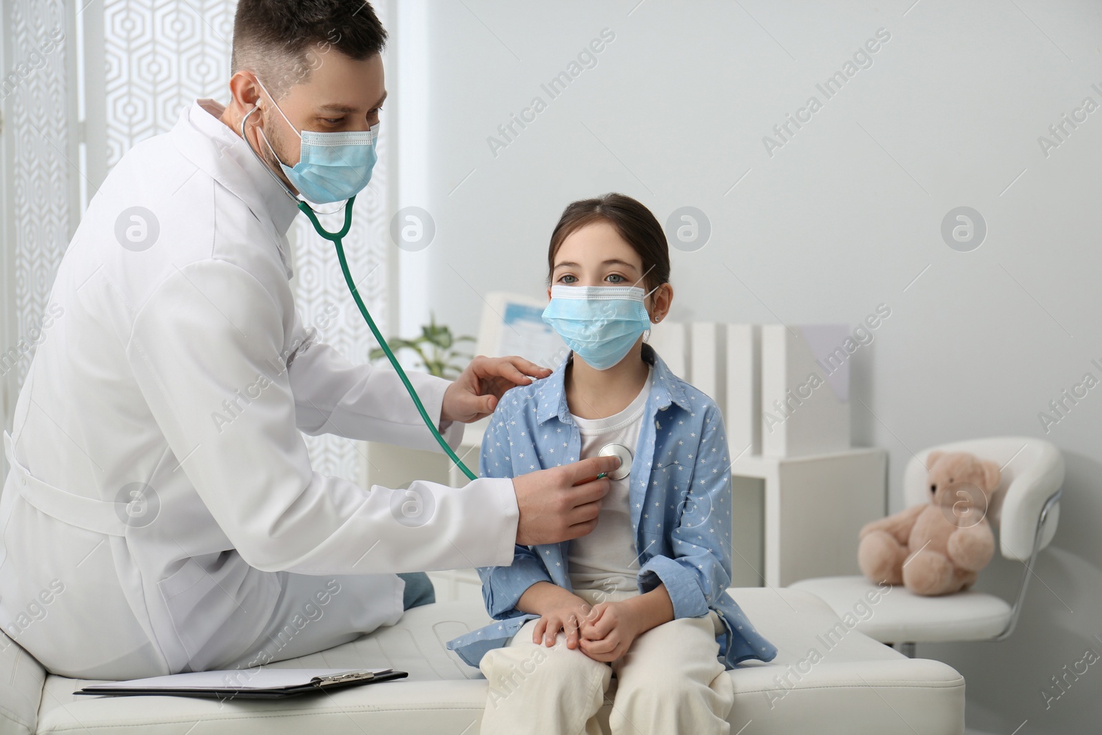 Photo of Pediatrician examining little girl in hospital. Doctor and patient wearing protective masks