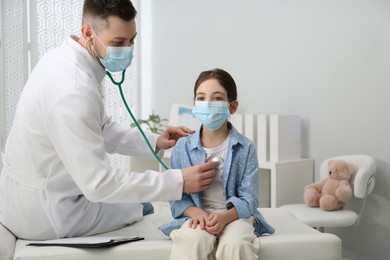 Pediatrician examining little girl in hospital. Doctor and patient wearing protective masks