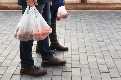 Photo of People carrying plastic bags with products outdoors, closeup. Space for text