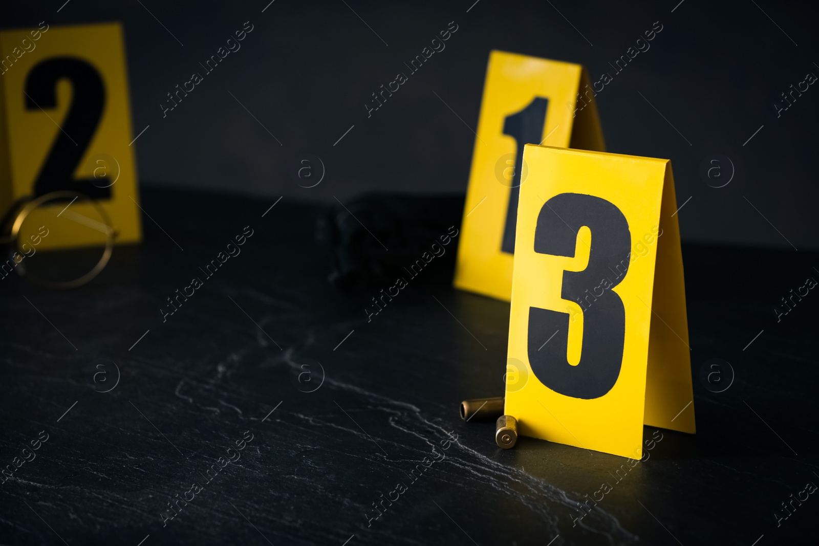 Photo of Shell casings and evidence marker on black slate table, closeup. Crime scene