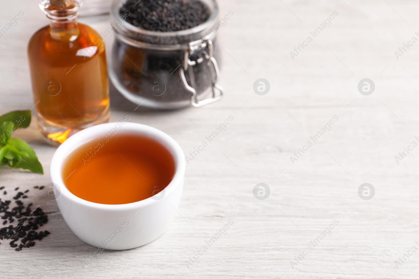 Photo of Fresh oil and black sesame seeds on light table, space for text