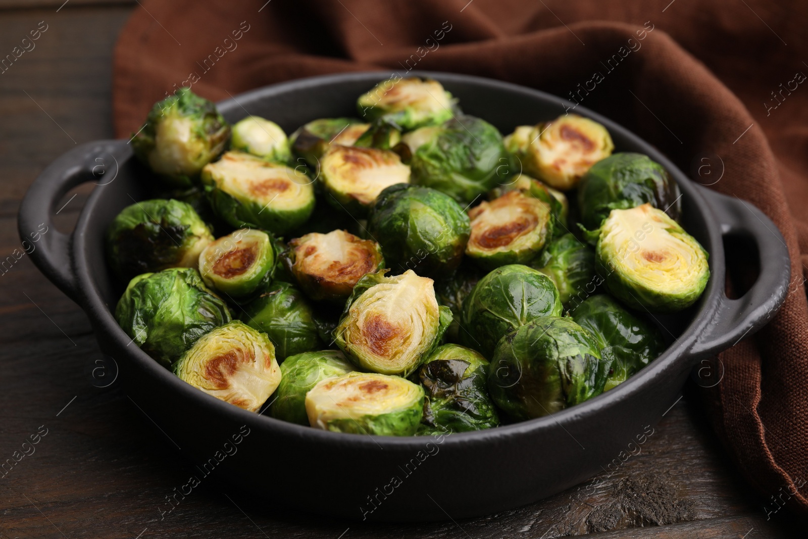 Photo of Delicious roasted Brussels sprouts in baking dish on wooden table, closeup