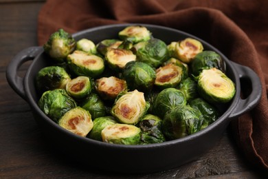 Photo of Delicious roasted Brussels sprouts in baking dish on wooden table, closeup