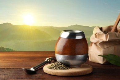 Image of Calabash with mate tea and bombilla on wooden table and beautiful view of mountain landscape, space for text