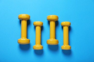 Photo of Yellow dumbbells on light blue background, flat lay. Morning exercise