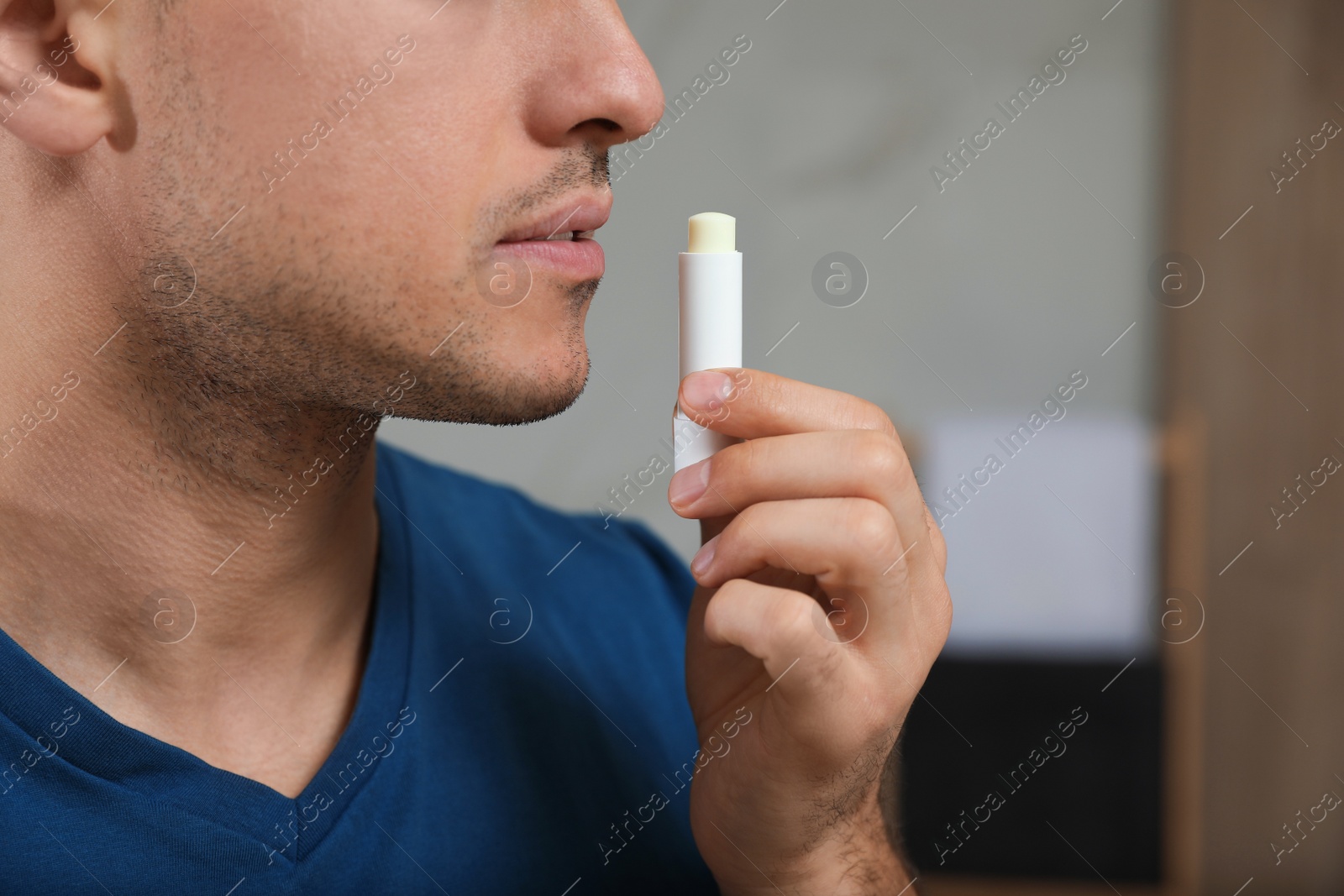 Photo of Man applying hygienic lip balm indoors, closeup