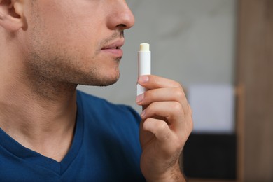 Photo of Man applying hygienic lip balm indoors, closeup