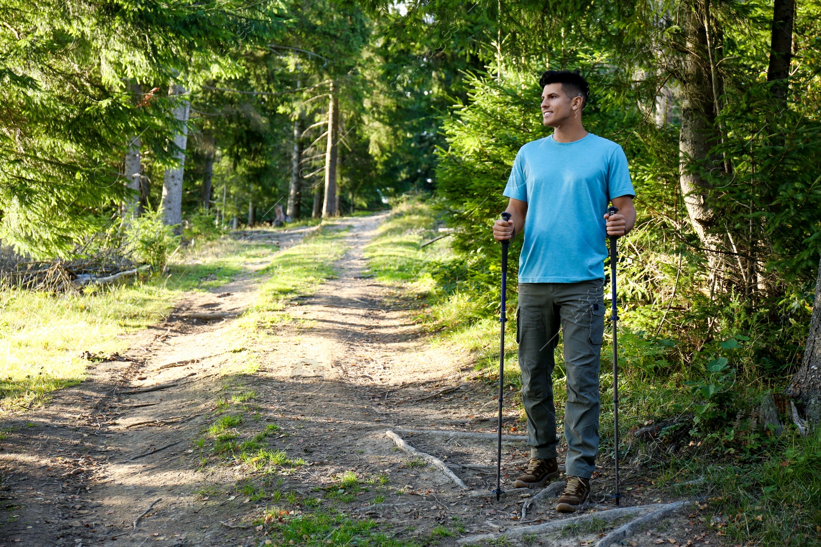 Photo of Man with trekking poles hiking in forest. Space for text