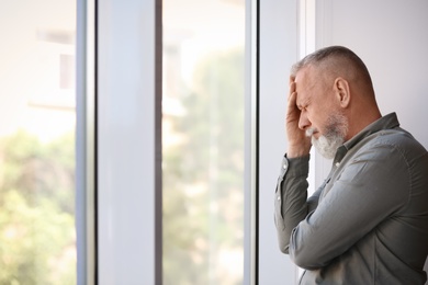 Depressed senior man near window indoors