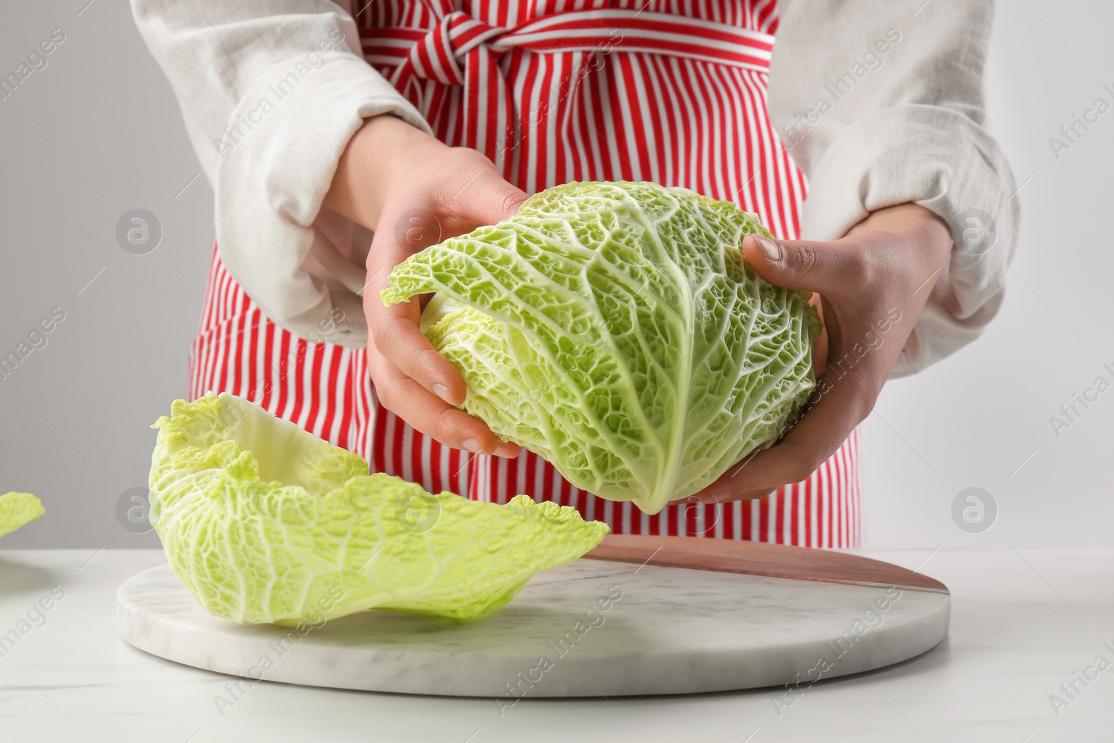 Photo of Woman separating leaf from fresh savoy cabbage at white marble table, closeup