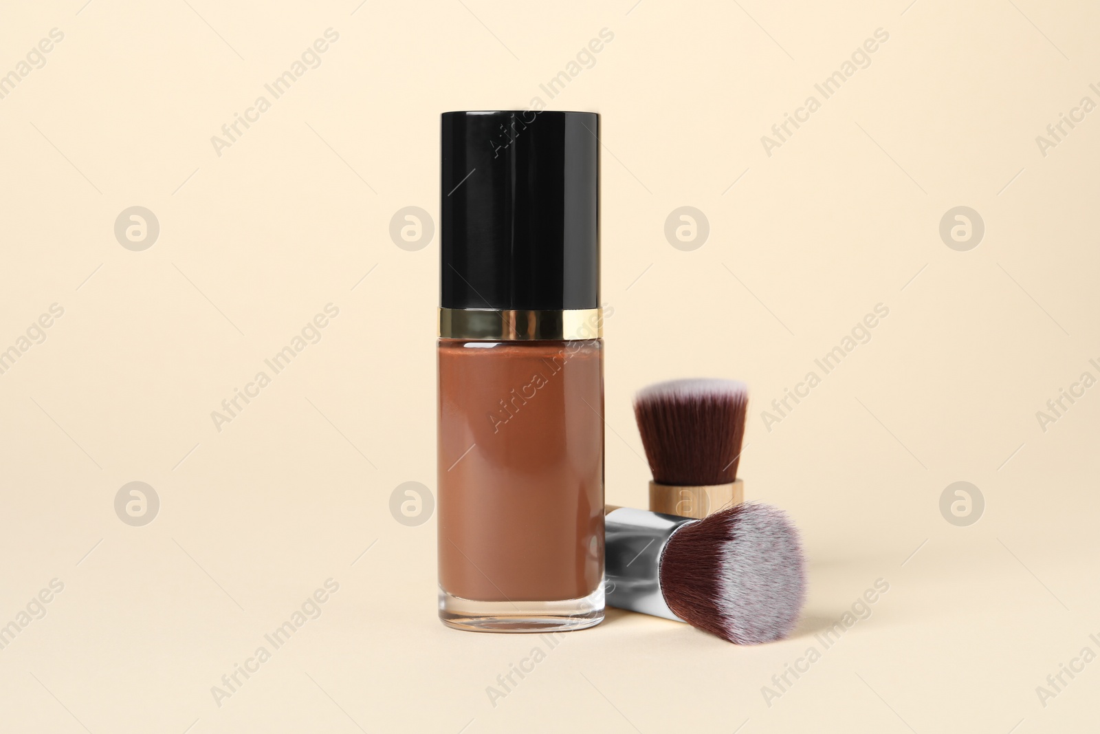 Photo of Bottle of skin foundation and brushes on beige background. Makeup product