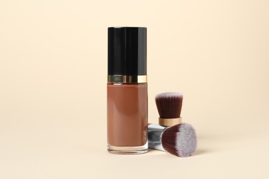 Photo of Bottle of skin foundation and brushes on beige background. Makeup product