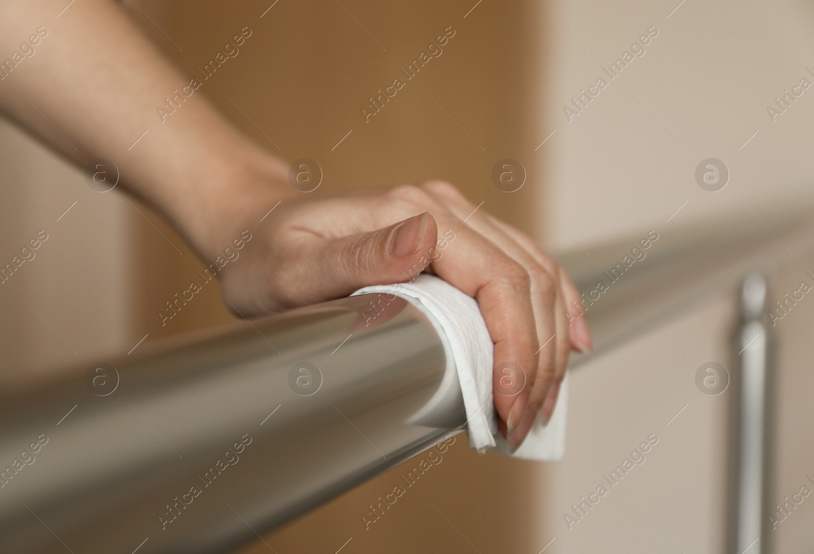 Photo of Woman cleaning metal railing with antiseptic wipe indoors, closeup