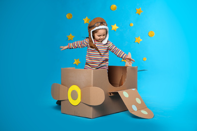 Little child playing with plane made of cardboard box near stars on blue background