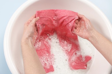 Woman washing baby clothes in basin on light blue background, closeup