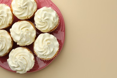 Tasty vanilla cupcakes with cream on beige background, top view. Space for text