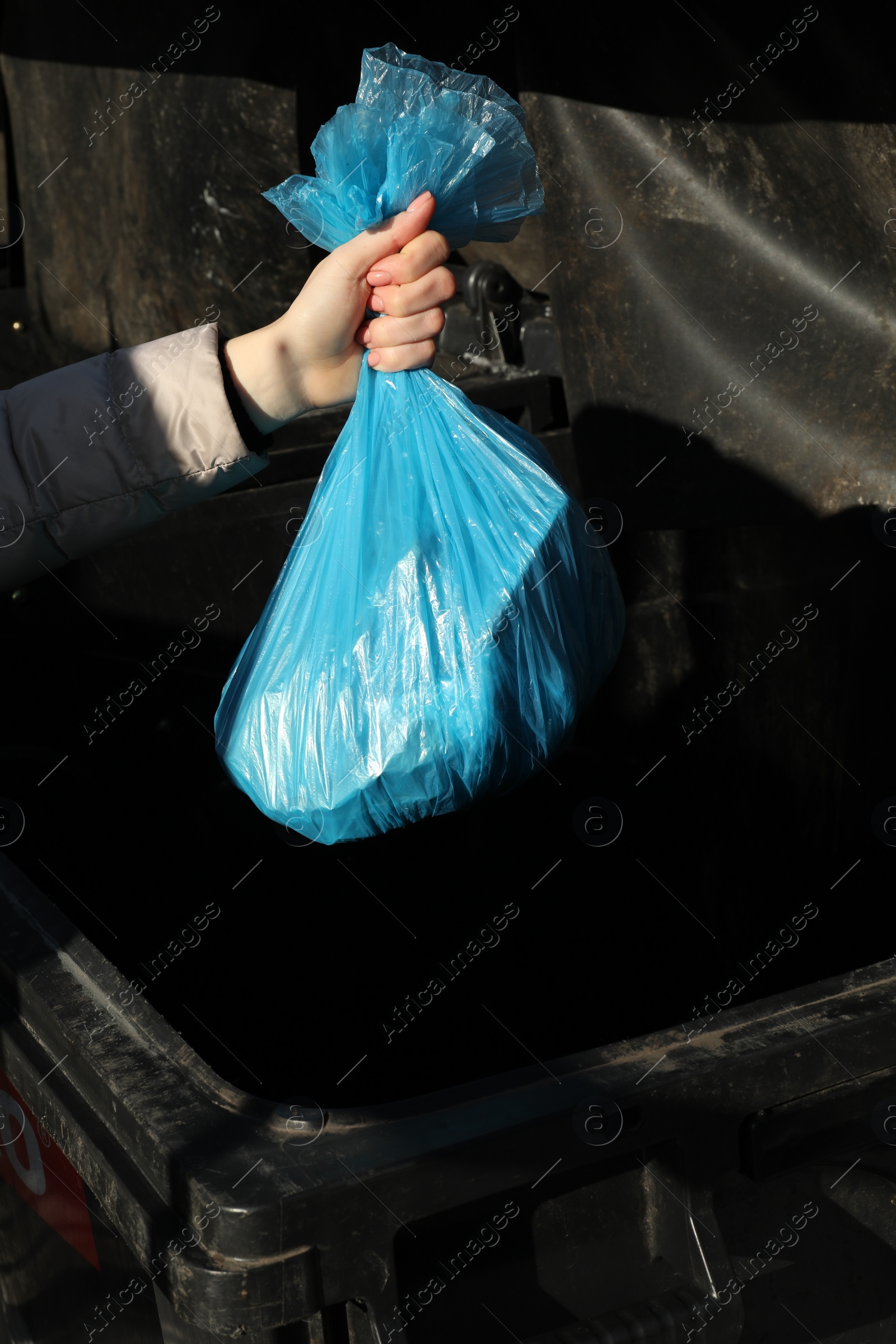 Photo of Woman throwing trash bag full of garbage in bin outdoors, closeup