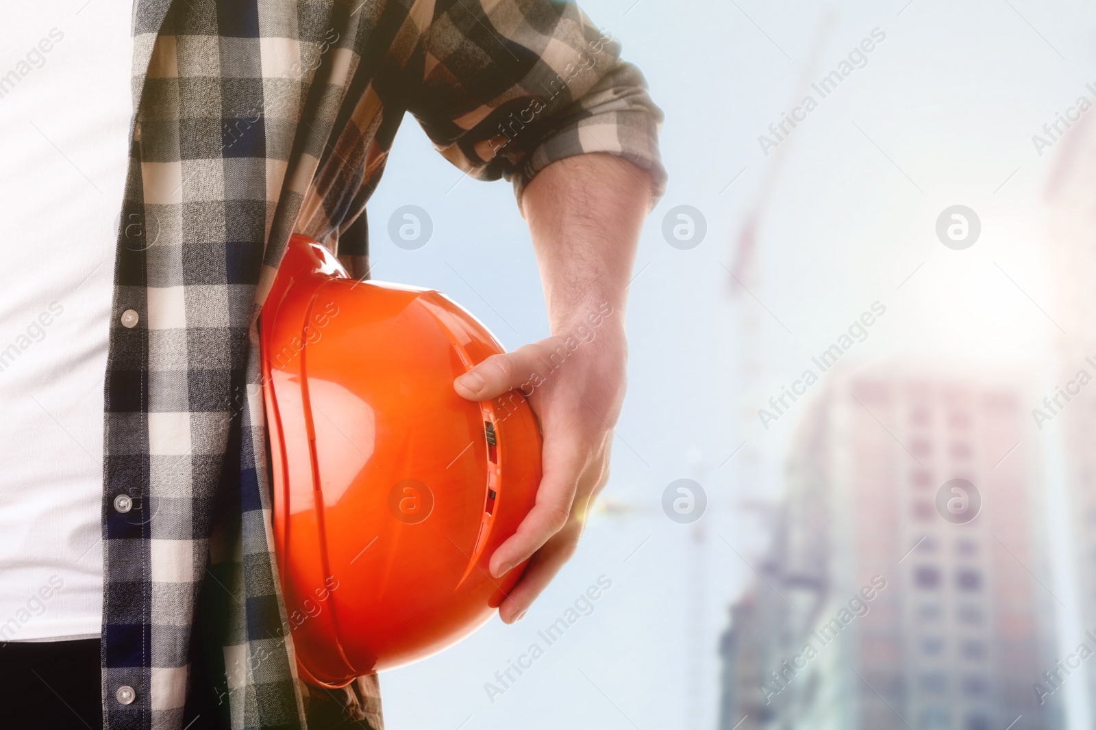 Image of Man with orange hard hat at construction site with unfinished building, closeup. Space for text 