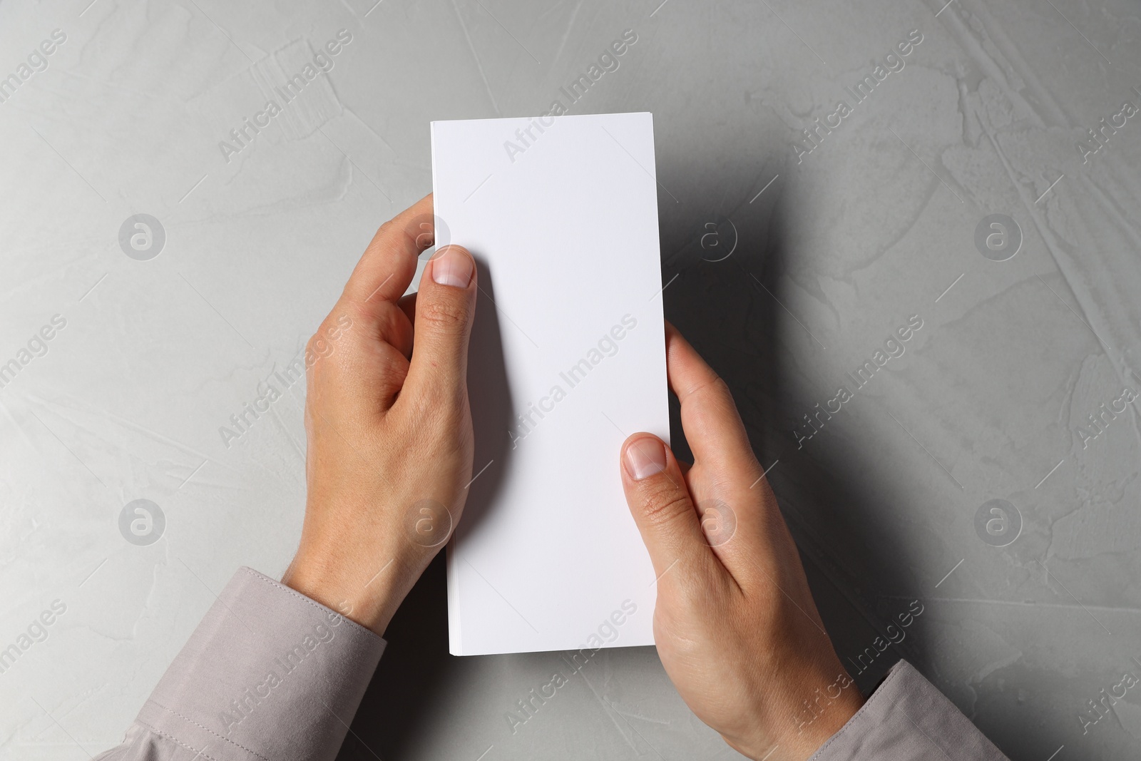 Photo of Man holding white blank card at light grey table, top view. Mockup for design