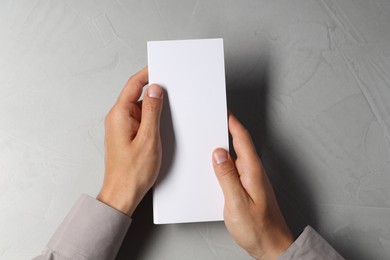 Photo of Man holding white blank card at light grey table, top view. Mockup for design