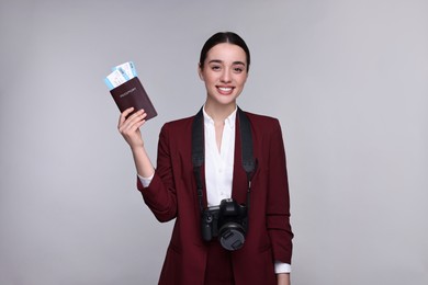 Smiling businesswoman with passport, tickets and camera on grey background