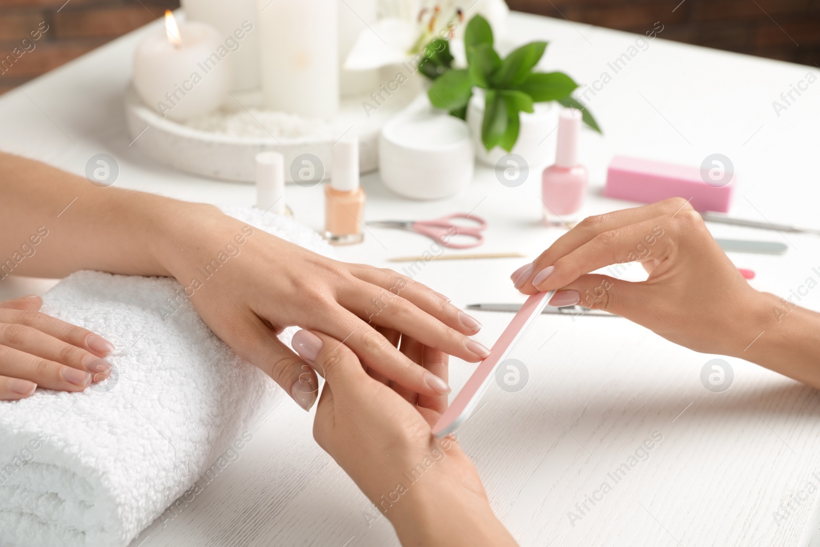 Photo of Manicurist filing client's nails at table, closeup. Spa treatment