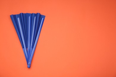 Photo of Bright blue hand fan on orange background, top view. Space for text