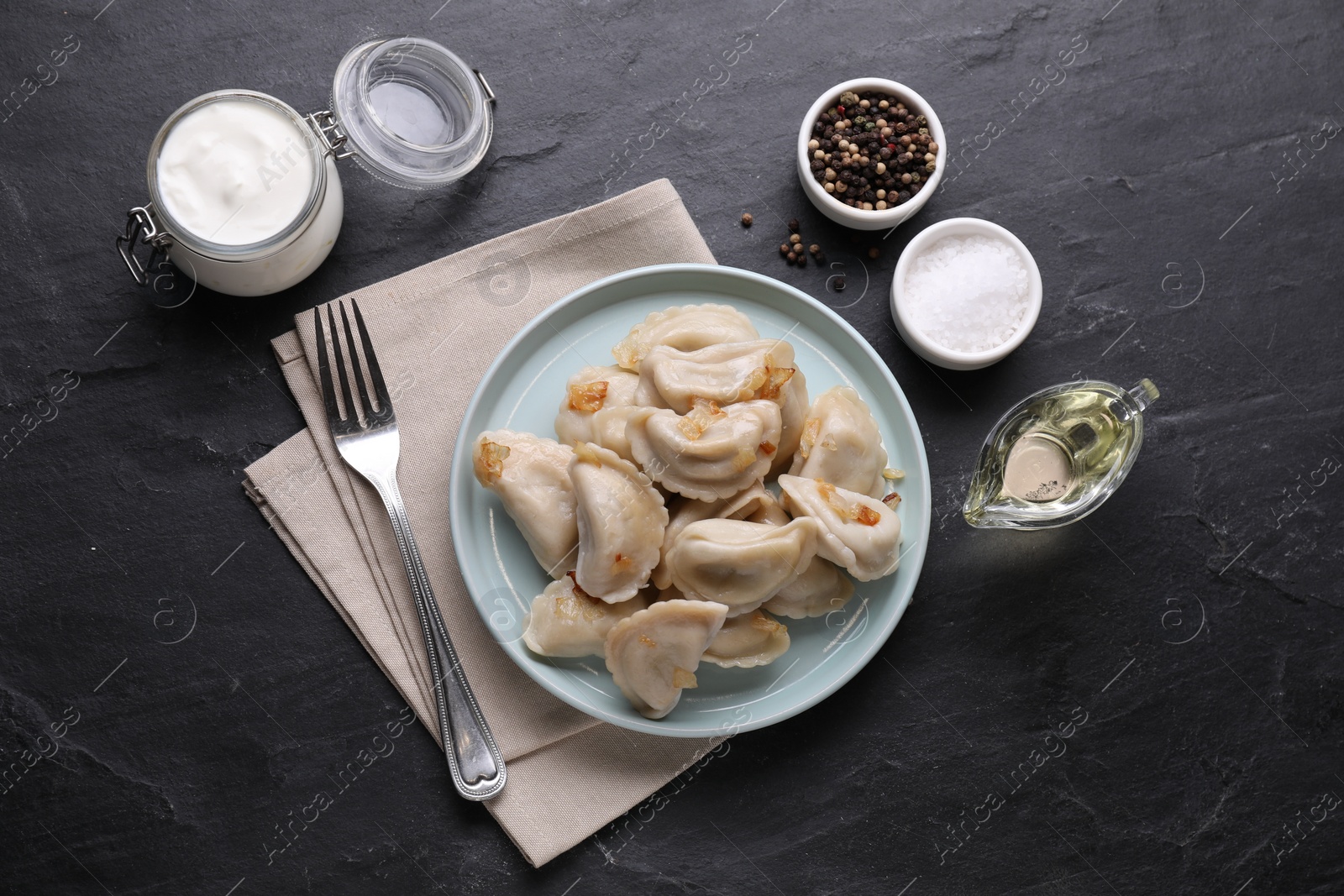 Photo of Delicious dumplings (varenyky) with potatoes and onion served on black table, flat lay