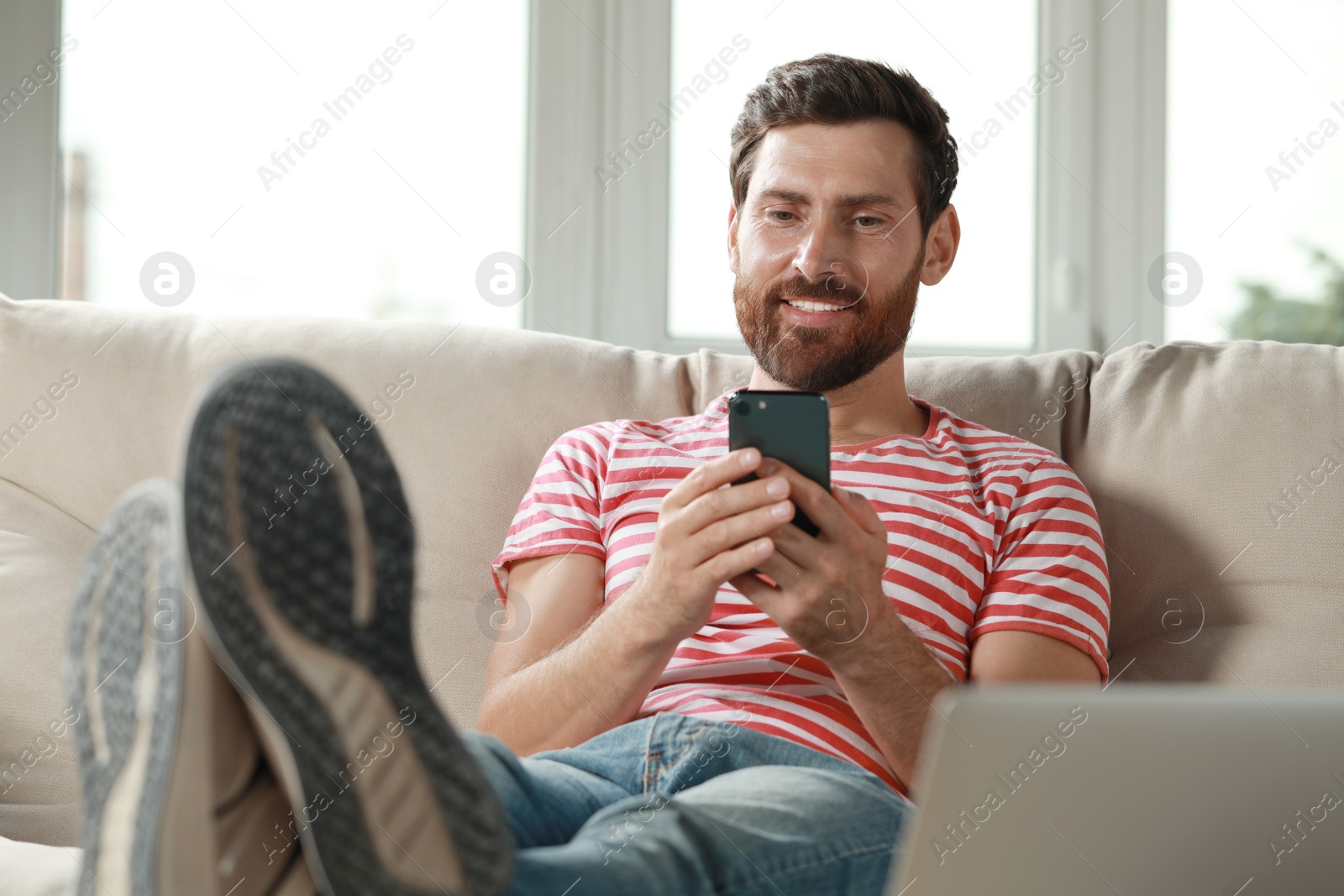 Photo of Handsome man using smartphone on sofa at home