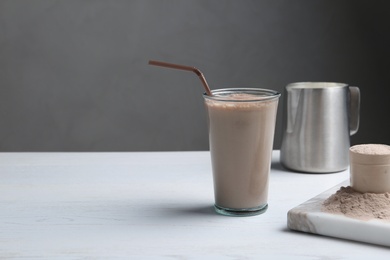 Photo of Glass with protein shake and scoop of powder on white wooden table. Space for text