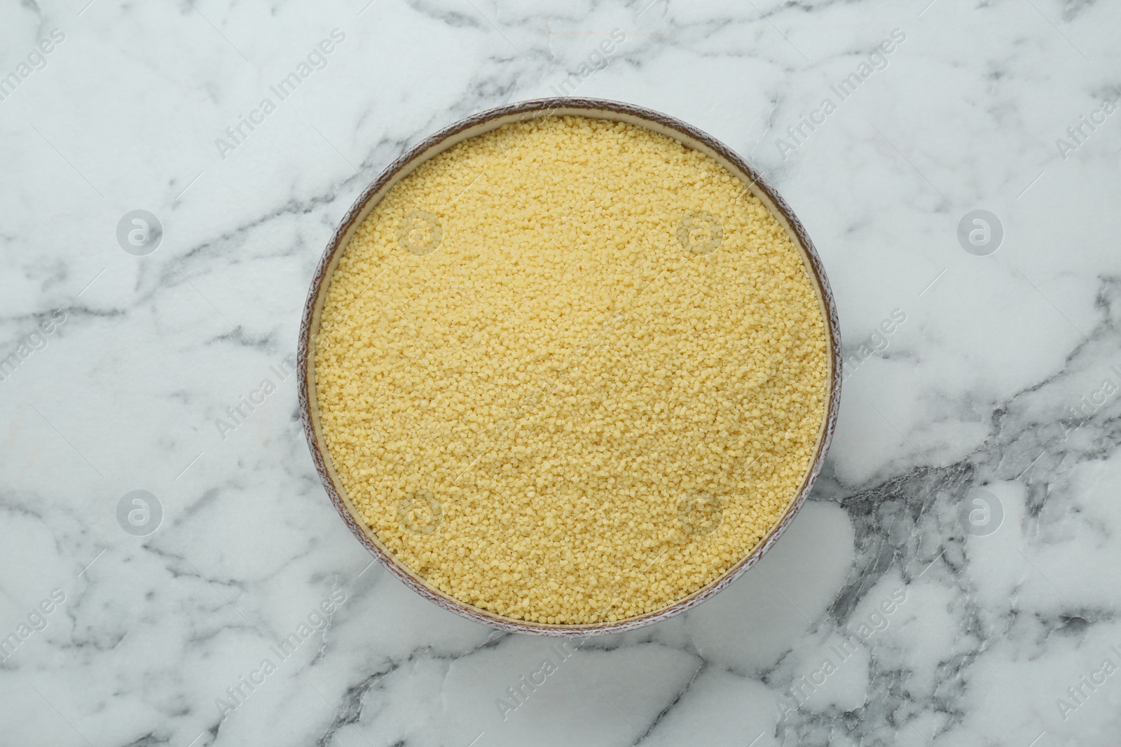 Photo of Bowl of raw couscous on white marble table, top view