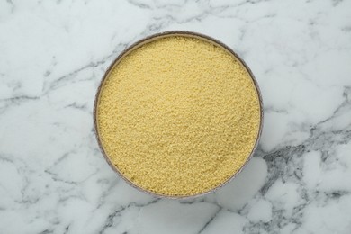 Photo of Bowl of raw couscous on white marble table, top view