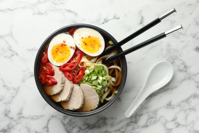 Photo of Delicious ramen in bowl and spoon on white marble table, flat lay. Noodle soup