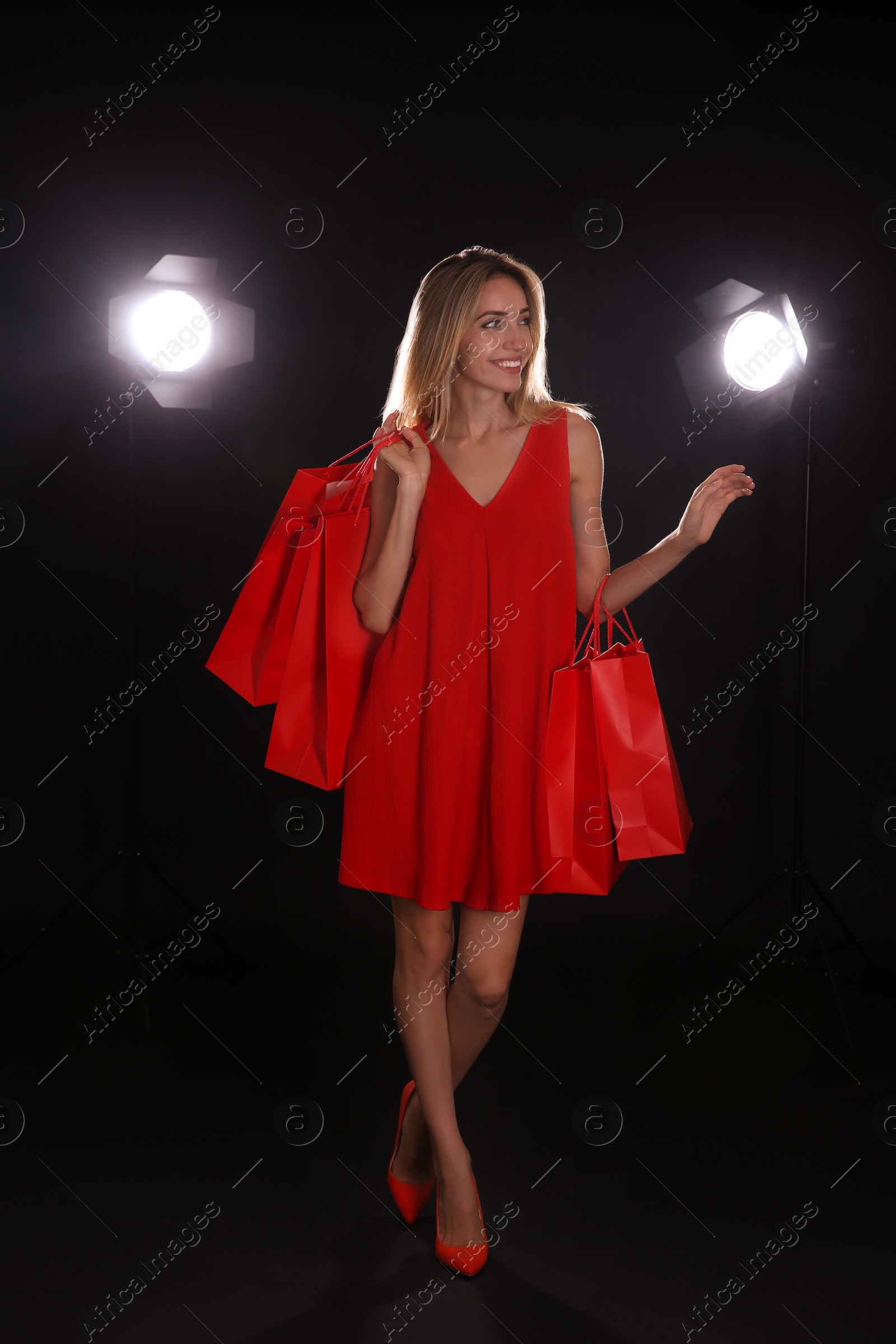 Photo of Happy young woman with shopping bags on dark background. Black Friday Sale