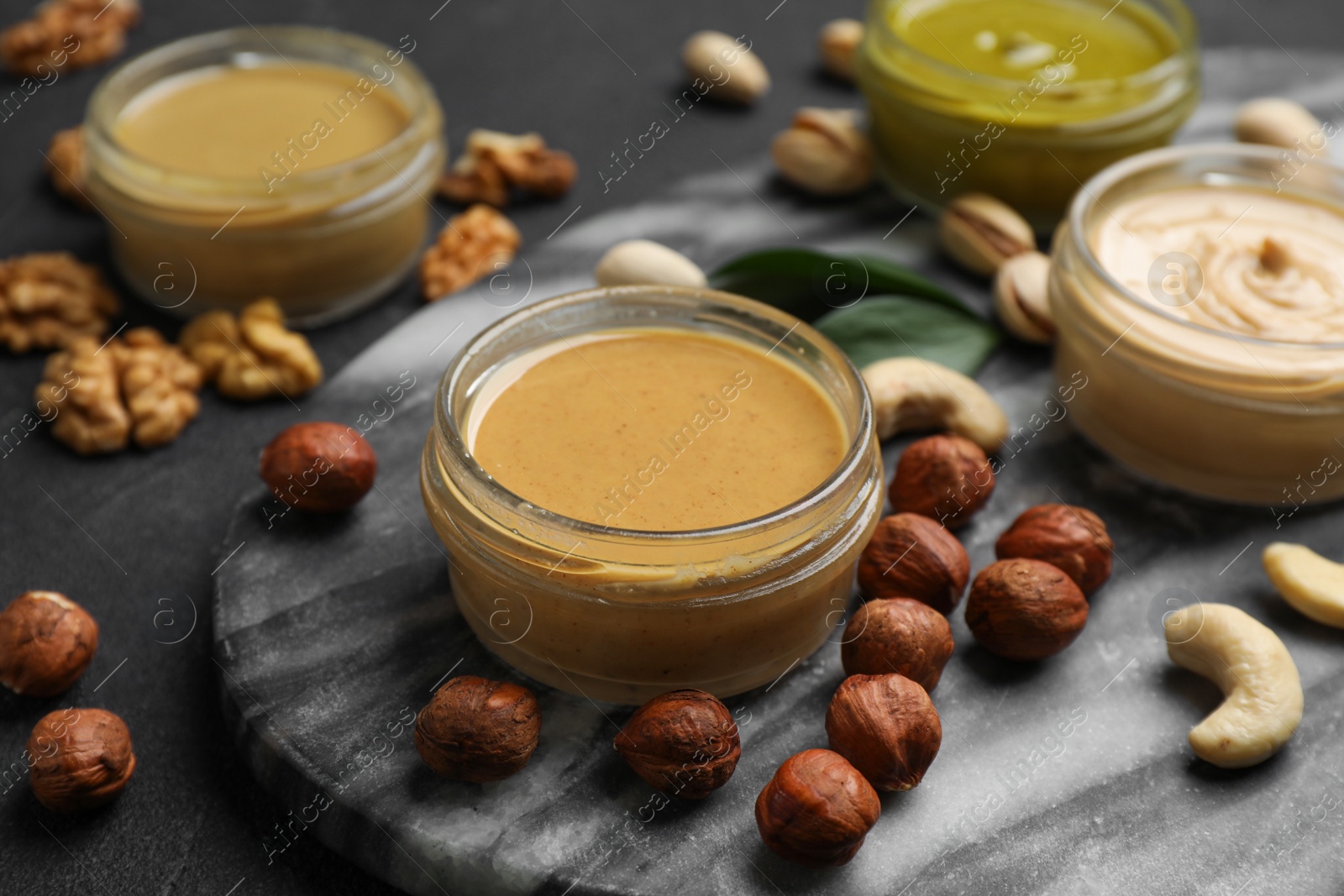 Photo of Jars with butters made of different nuts and ingredients on black table, closeup