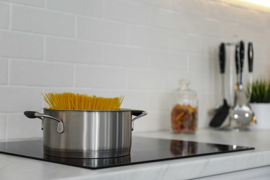 Photo of Saucepan with uncooked pasta on stove in kitchen